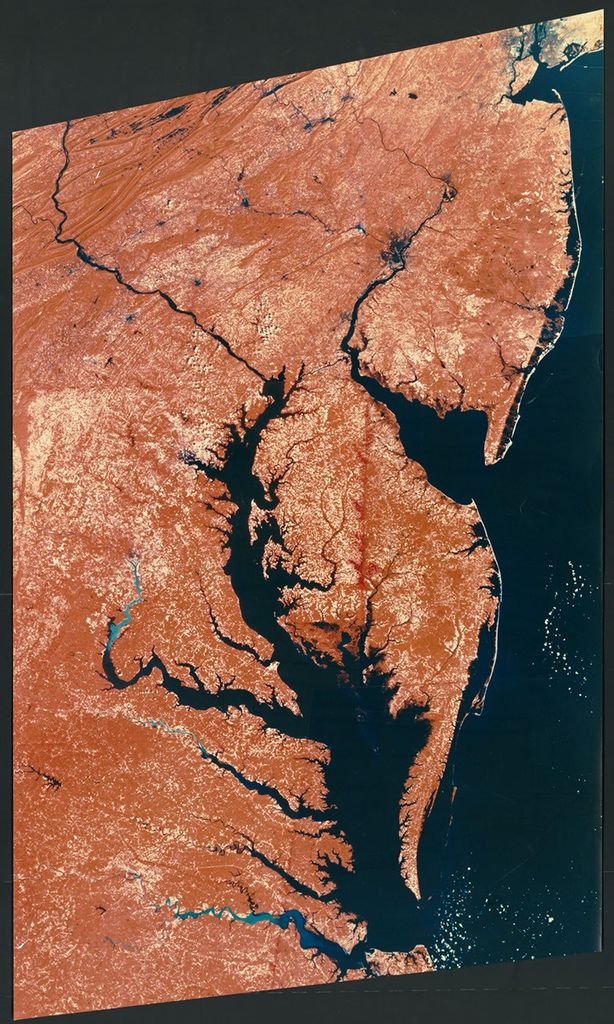 A false-color Landsat satellite image from 1977 showing the Middle Atlantic States region of the United States. The image covers an area from New York City to Hampton Roads, Virginia, displaying the distinctive coastal features, major water bodies, and land cover patterns. Vegetation appears in reddish tones, water bodies in dark blue, and developed areas in lighter colors.