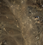 Aerial satellite image of Yucca Flat in Nevada showing numerous circular subsidence craters scattered across an arid desert landscape. The craters appear as distinct circular depressions against the brown desert terrain, with mountainous features visible on the right edge of the image.