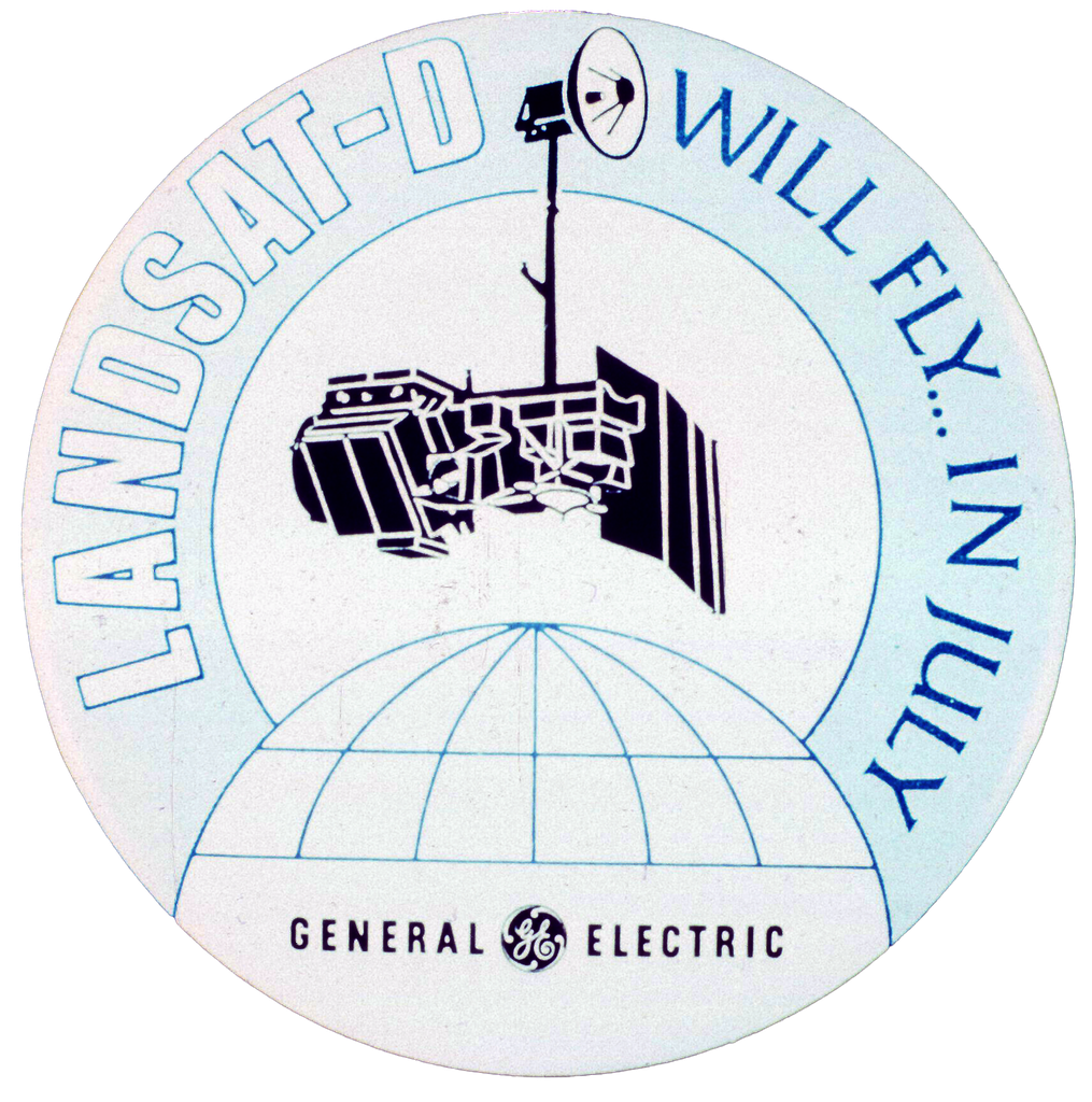 A Landsat-D mission patch with the text "Landsat-D Will Fly... In July" and "General Electric" written below.