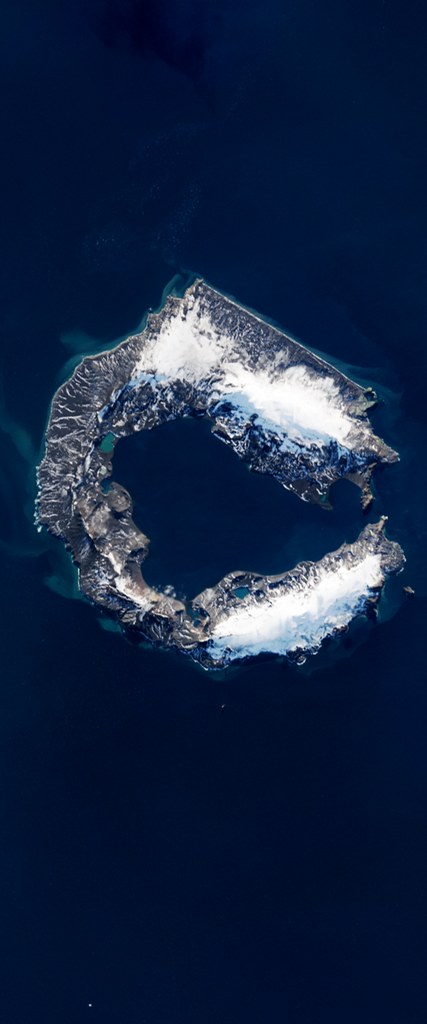 Landsat satellite image of a mountainous island forming the lower case letter C. The island is covered by snow and ice on the upper and lower right portions.