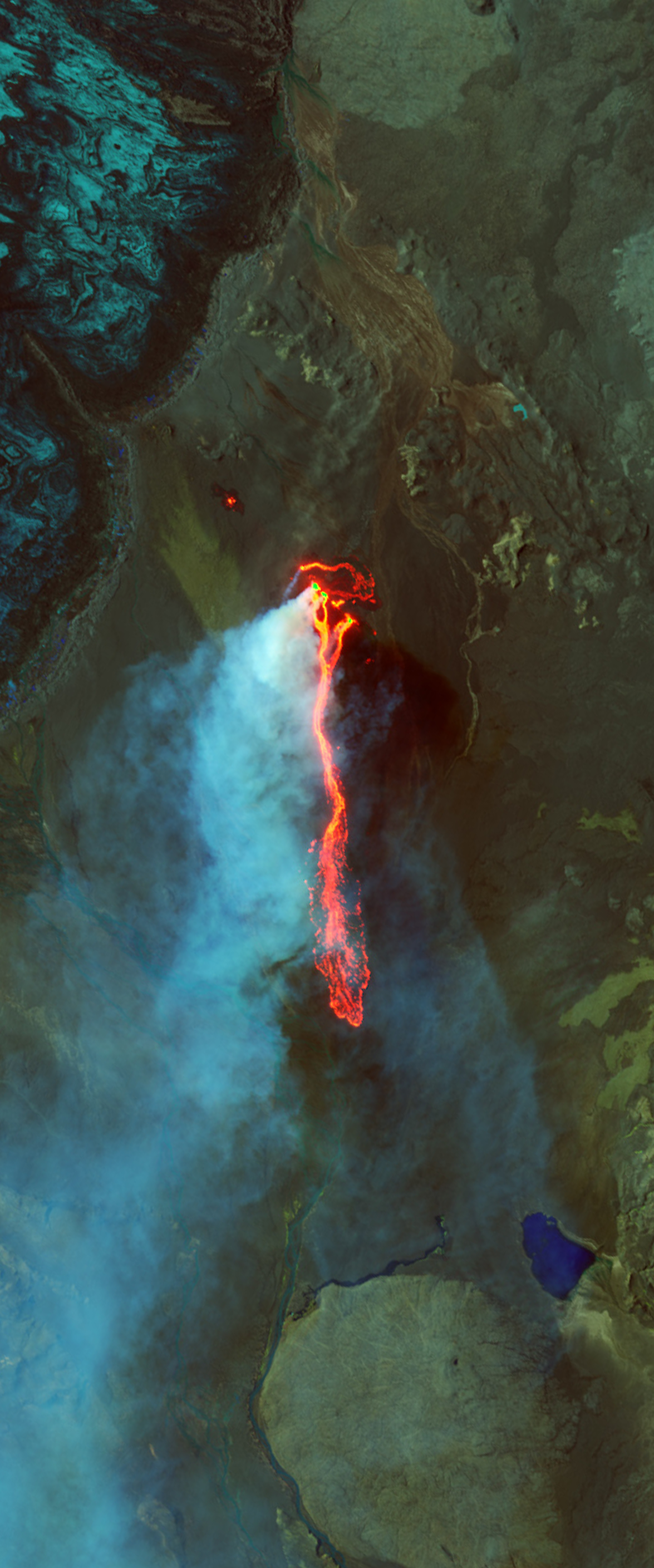 Landsat satellite image of a lava field shown in the color red form a lower case letter I. Ice and the plume of steam are shown in the color light blue and are flowing out to the left of the lava field.