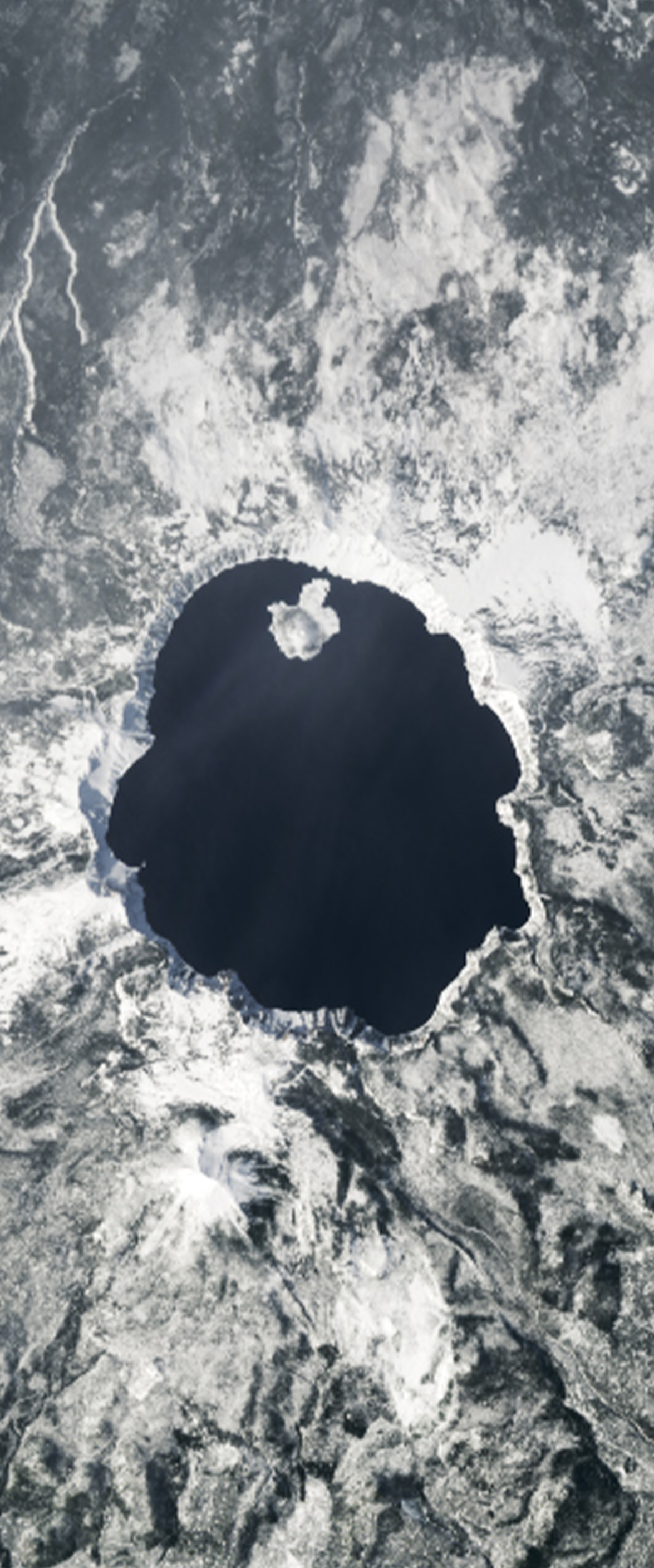 Lake surrounded by snow on top of a mountain forms the letter O in this Landsat satellite image.