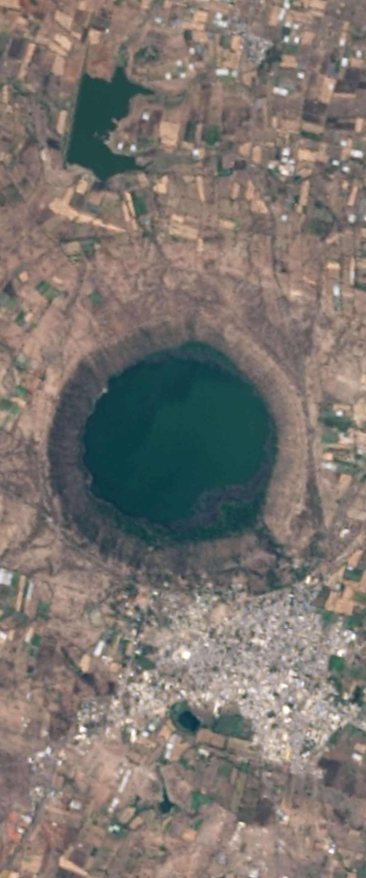 Landsat satellite image of a water filled crater in the shape of the capital letter Q.