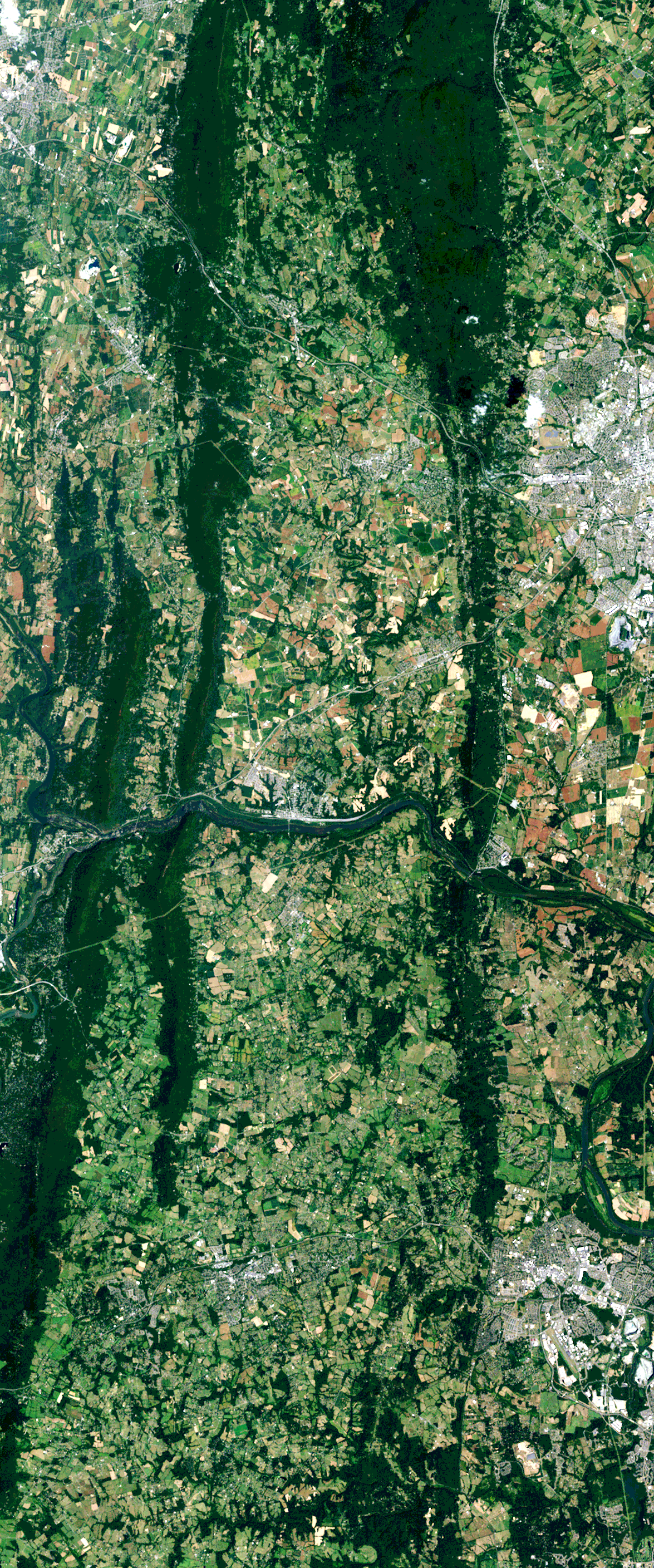 Landsat satellite image of dark forested ridges and a river surrounded by lighter green and brown agricultural fields forms the uppercase letter H.