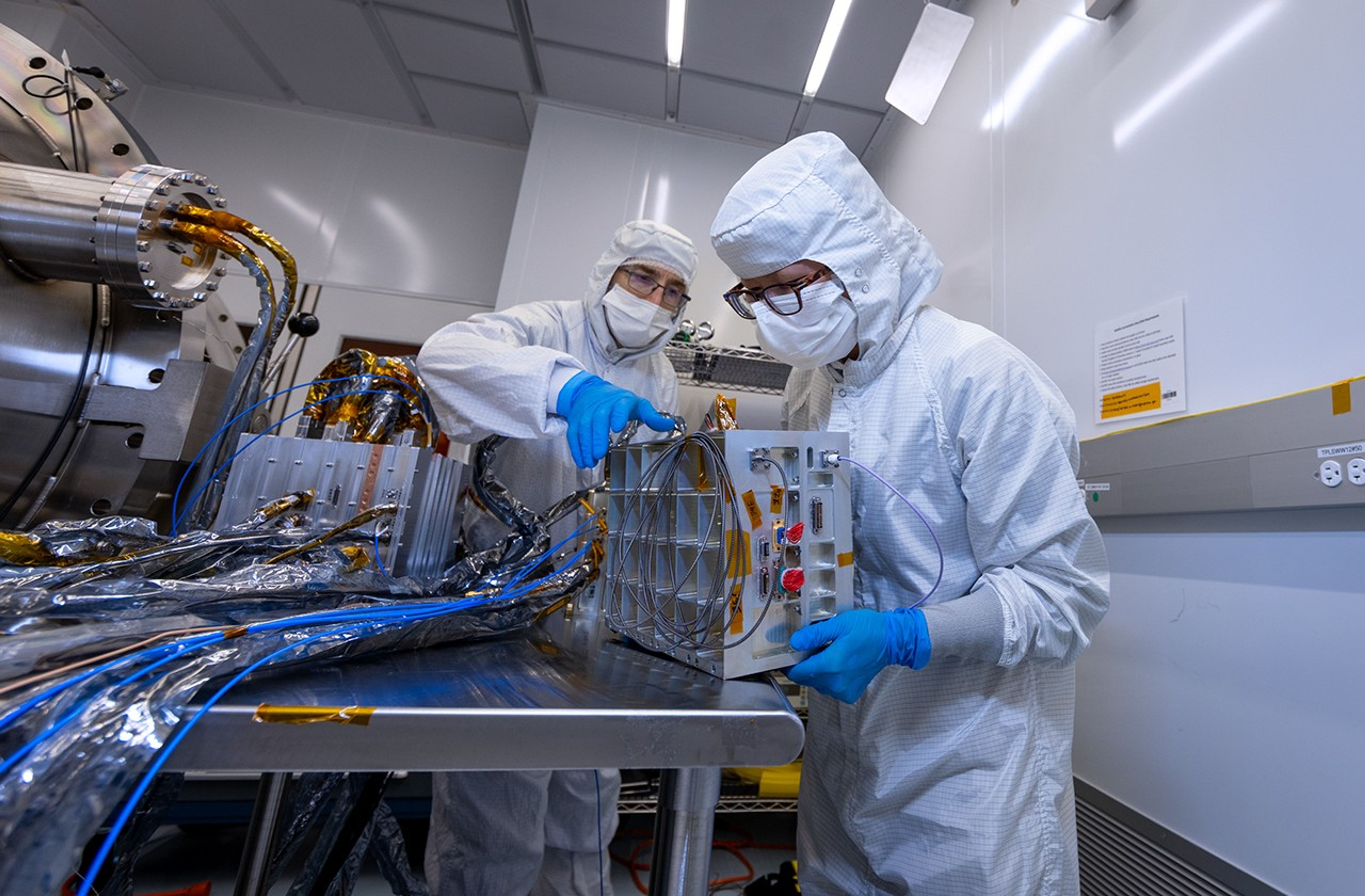 Two people work on a silver box in a lab.