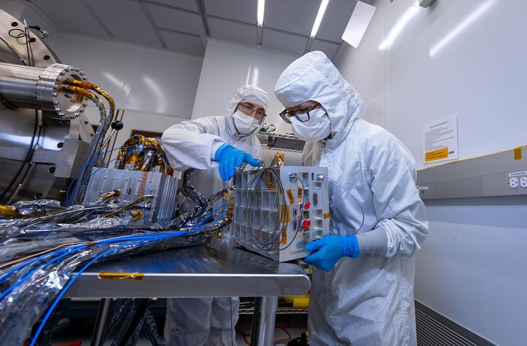 Two people work on a silver box in a lab.
