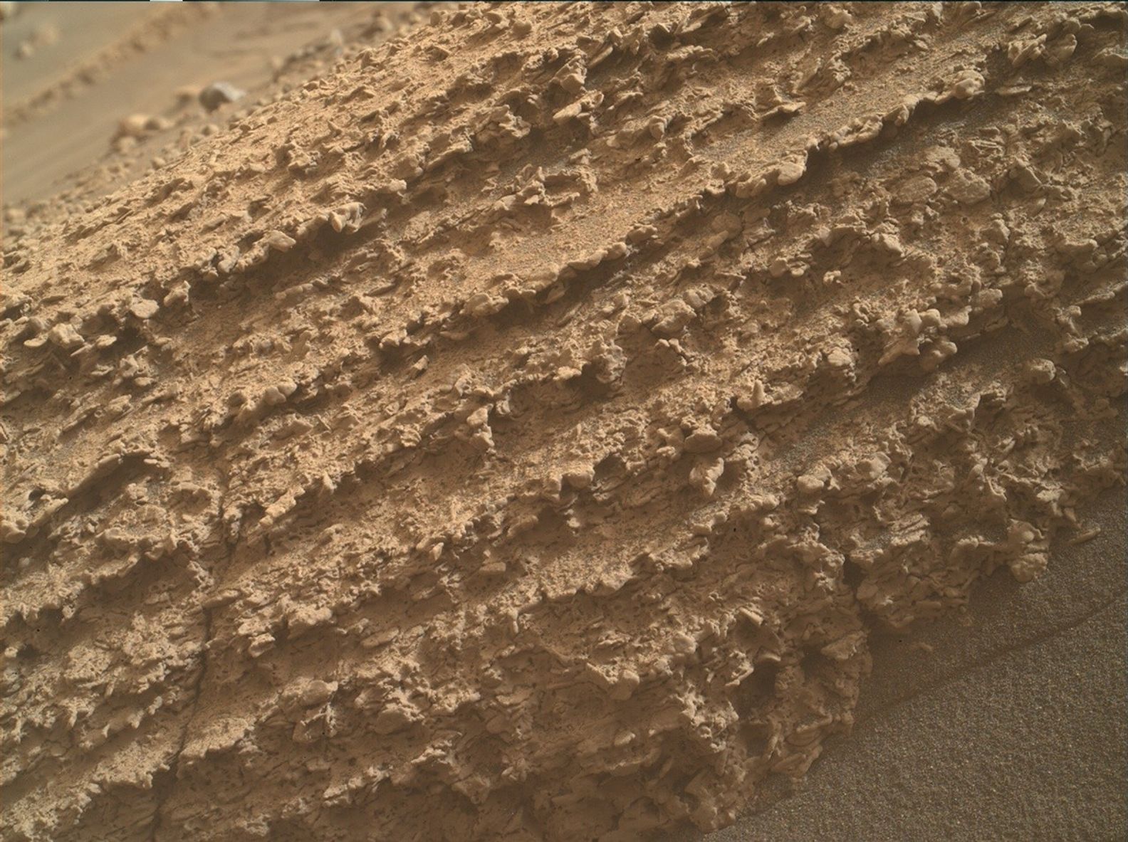 A close-up color photo of terrain on Mars shows a mounded spread of what looks like whipped chunky peanut butter, in color and consistency, covering almost all of the frame from upper right to lower left. Two small triangles in the upper left and lower right corners of the frame show the fine sand that borders either side of the other material.