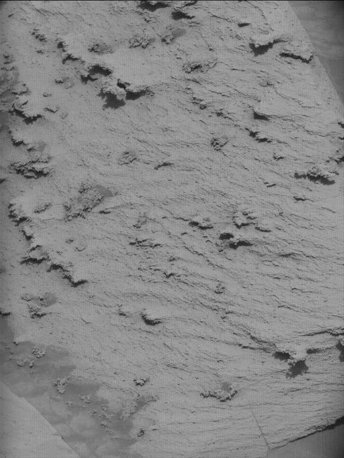 A grayscale image shows a patch of rough, slightly wavy terrain with several flat, jagged areas emerging from the surface and all pointing toward the lower left corner of the frame. The area looks like a patch of peanut butter or frosting, with wavy lines and peaks left by a spreader.