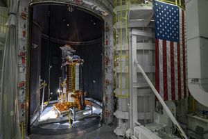 NISAR's flight antenna undergoes testing at NASA's Jet Propulsion Laboratory. The structure stands beyond the open bay doors of a large thermal vacuum chamber. The American flag hangs to the right of the door.