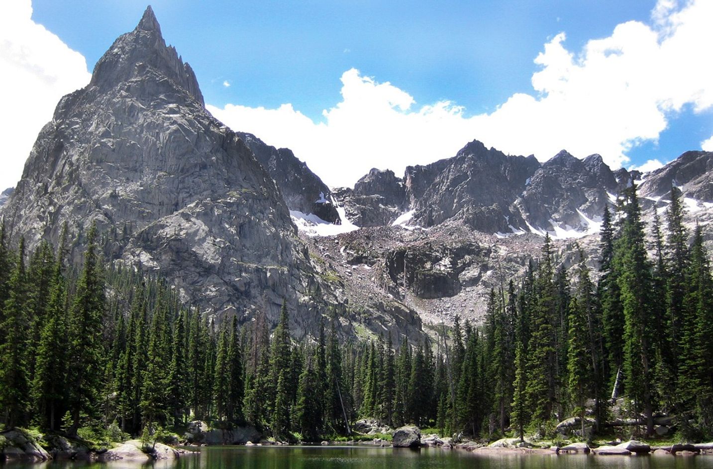 The rocky mountains soar in the background just behind the nearby forest along the edge of the lake.