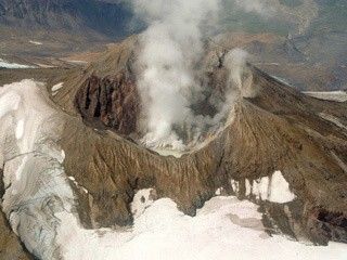 A pool of steaming water resides in this volcanic crater while glacial snow pack surrounds the hot volcano.