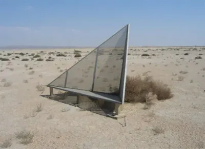a triangular structure stands on a platform in the middle of the desert.