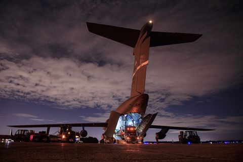 A large, dimly lit plane is seen from behind at night. The back end is open and lights are on…