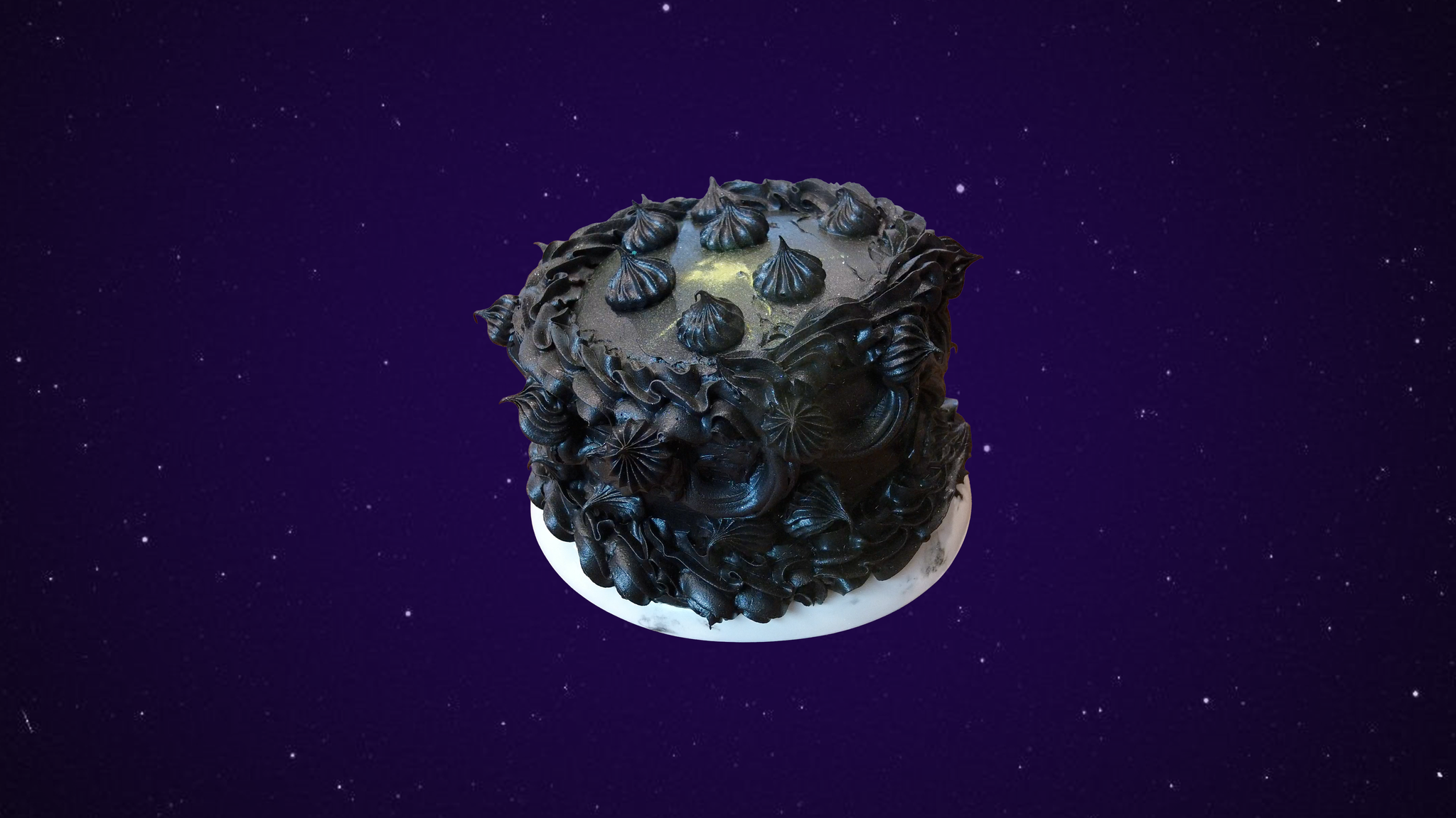 A black cake with an excess of black piping covered shimmering gold dust on a white plate in front of a starry background covered in purple haze.