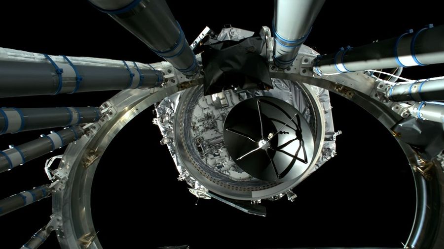 View from the rocket’s upper stage showing the spacecraft emerging after separation, framed by structural support arms and metallic wiring against the blackness of space.