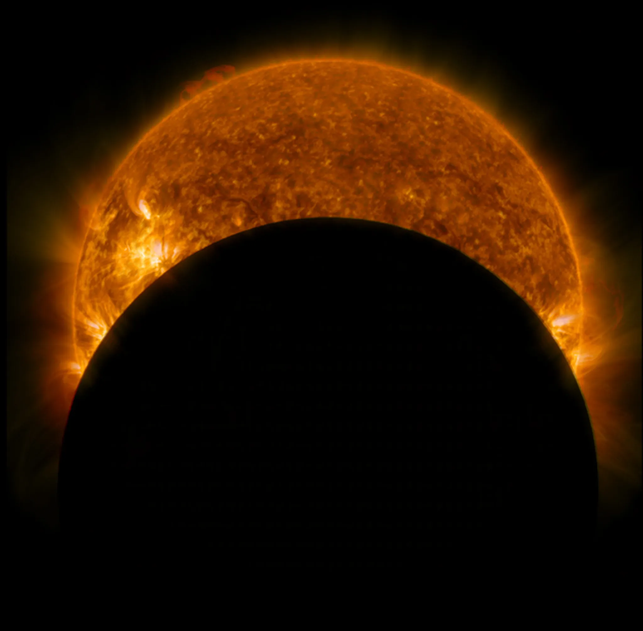 A solar eclipse viewed from space, showing the Moon partially covering the Sun. The Sun's fiery surface and corona are visible, creating a glowing halo around the dark silhouette of the Moon.