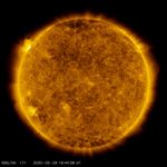 Una imagen satelital del Sol, coloreada en dorado. Un punto brillante de luz se encuentra sobre el horizonte izquierdo.