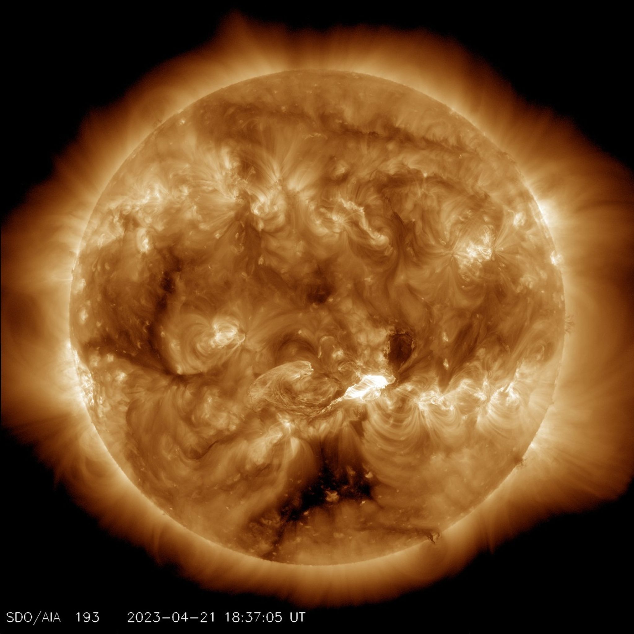 The Sun appears in shades of gold with some brighter and darker regions, set against a black background. In the lower right part of the Sun is a bright flash of white, a solar flare.
