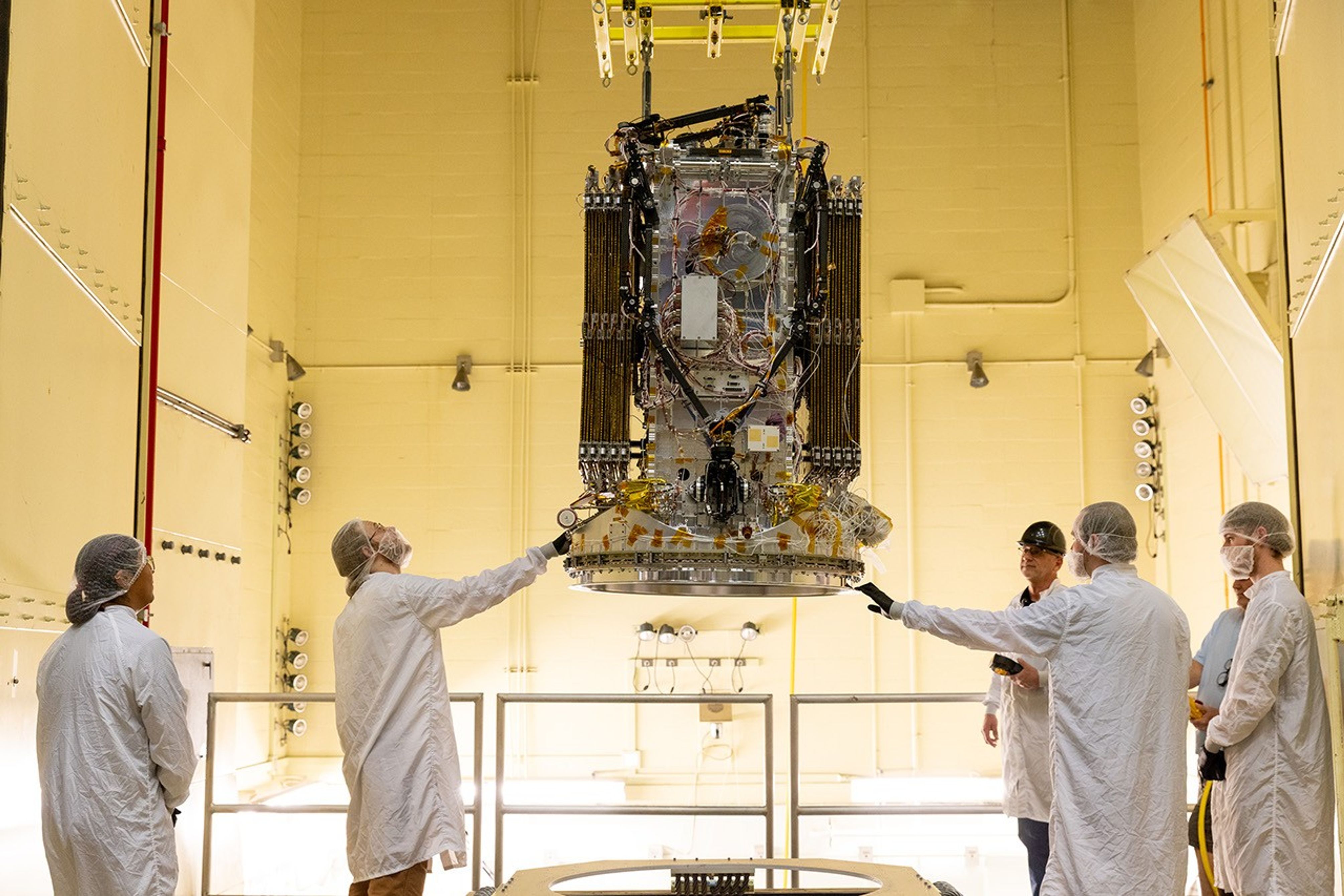 People maneuver a spacecraft into a large chamber.