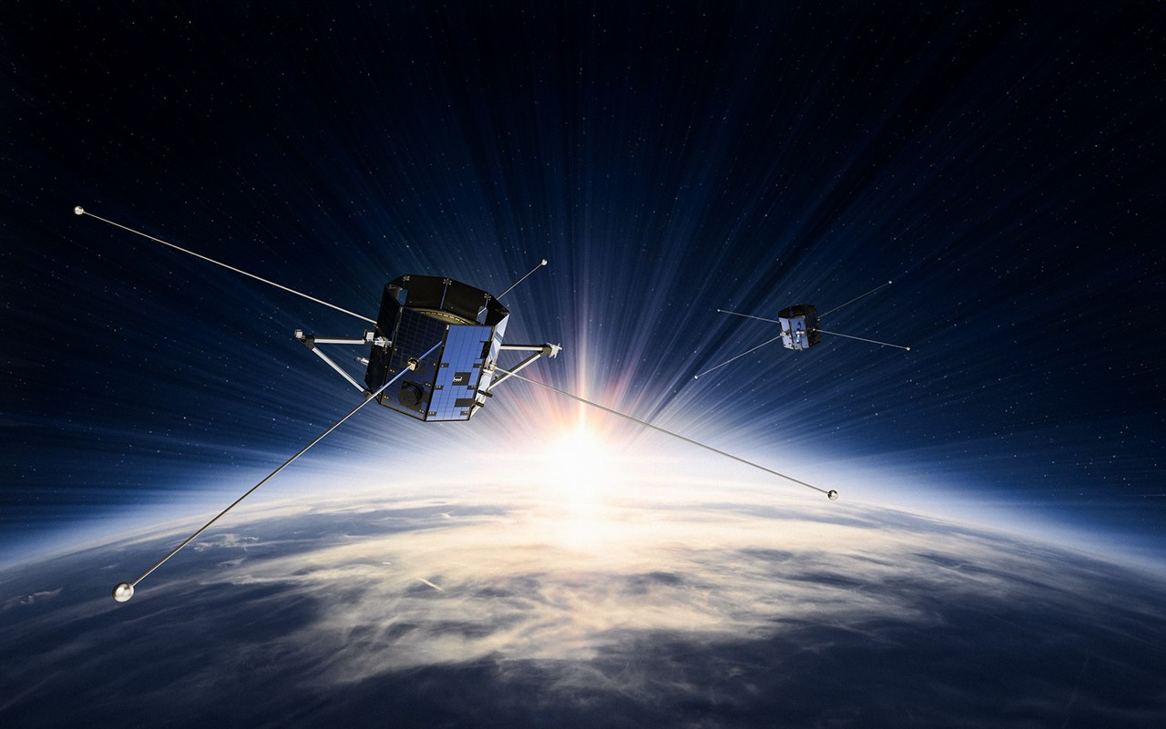 An illustration showing the 2 TRACERS spacecraft. Filling the bottom half of the landscape image is a cloudy Earth. Behind Earth, the bright Sun is peaking out, filling the dark expanse of space with streaks of white light. The two spacecraft orbit above Earth, large hexagonal cylinders with long poles sticking out horizontally in 4 directions.