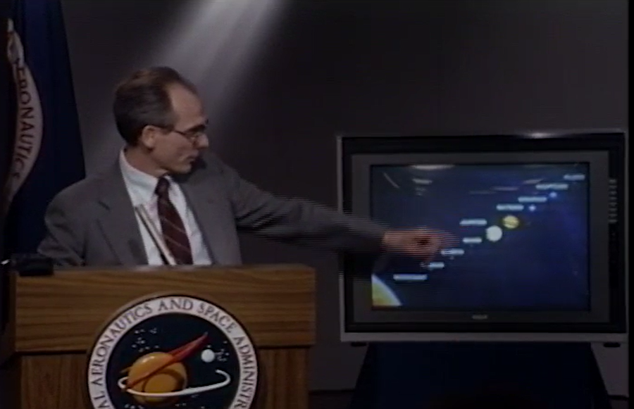 Ed Stone pointing to a screen depicting the solar system in a 1990 press conference