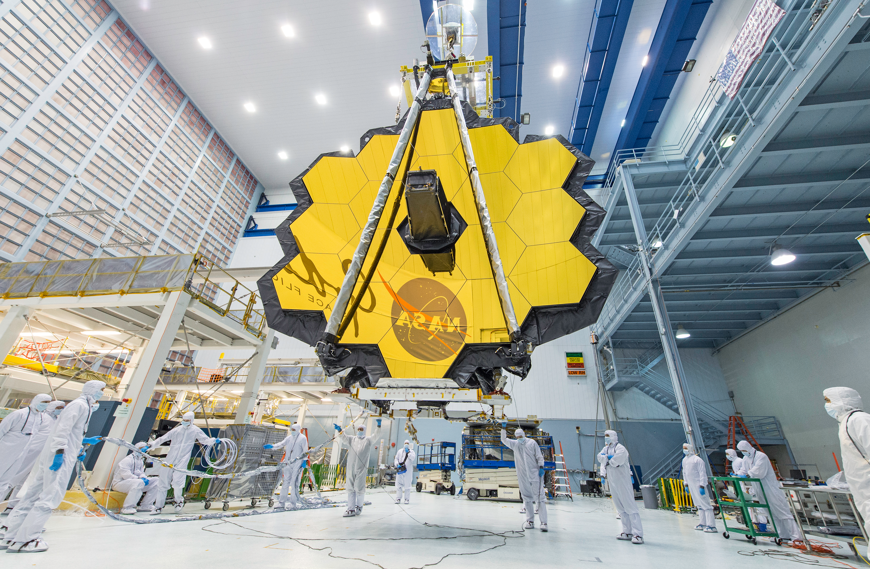 In the center of a clean room is Webb’s primary mirror, which has 18 hexagonal, gold-colored segments, and secondary mirror, supported by two thin, gray struts.