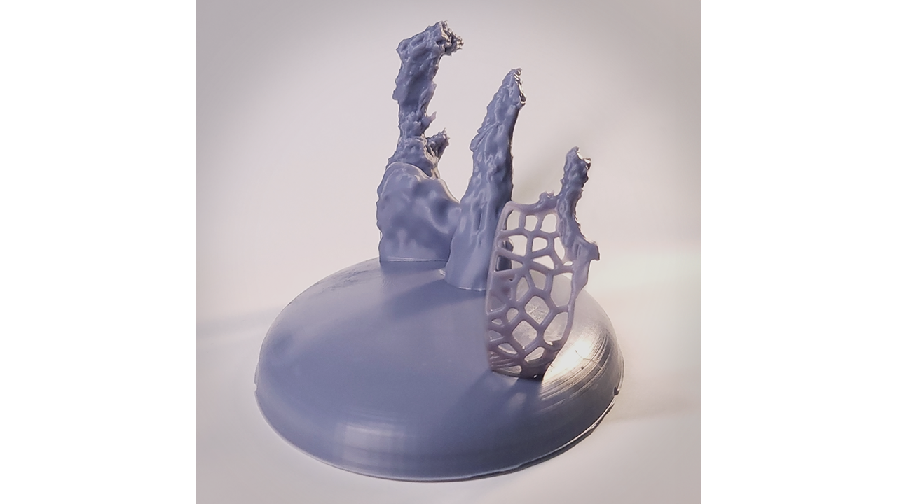 Photograph of a 3D printed model of the Pillars of Creation. The model is light gray with a silk-like texture, and the background is white. The three pillars rise up from a base that has a pancake-dome shape. The base is rotated about 60 degrees clockwise from the typical left-to-right orientation: The tallest pillar is at the back left at about 11 o’clock; the shortest is in the foreground right, at about 5 o’clock. The model is lit from several different angles to highlight the details. The pillars cast faint shadows toward the lower left. The pillars are craggy and stalagmite-like. The surfaces are smooth in some places, and pitted and grooved in others. Some edges are rounded and some appear sharp and jagged. The tall pillar at the back left and the middle pillar are solid all the way to the base. The small pillar at the front right is connected to the base by a web-like lattice made out of the same material as the rest of the model.