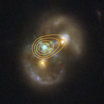 A pair of distant galaxies that form the rough shape of an infinity symbol seen at roughly a 45-degree angle. Two overlapping, fuzzy rings with brighter blue patches are at upper right and lower left. At the center of each ring is a bright yellow blob, which is the nucleus. Where the two rings overlap on the left side, there is a mottled green patch of glowing gas midway between the two yellow nuclei. It is offset slightly to the left. Orange contours are overlaid on the galaxies. The contours are egg-shaped and centered on the green patch between the two galaxies.