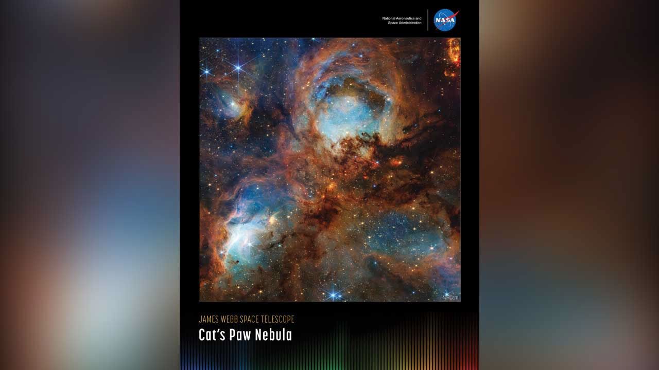 A vertically oriented poster with an image of the Cat’s Paw Nebula against a black background. Four roughly circular areas are toward the center of the frame: a small oval toward the top left, a large circle in the top center, and two ovals at bottom left and right. Each circular area, surrounded by brown filaments, glows a luminous blue. Toward the center are small, fiery red clumps scattered among the brown dust. Many yellow stars are spread throughout. Along the bottom is a series of thin vertical bars ranging from purple at left to blue, green, yellow, orange, and red at right. Bars are separated slightly, with black in between. Bar colors are brightest at the bottom, fading up to black. Brightness varies from bar to bar, giving the array an undulating feel. At upper right is text that reads, “National Aeronautics and Space Administration” and NASA’s blue, white, and red meatball insignia. Title text appears at lower left that says, “James Webb Space Telescope: Cat’s Paw Nebula.”