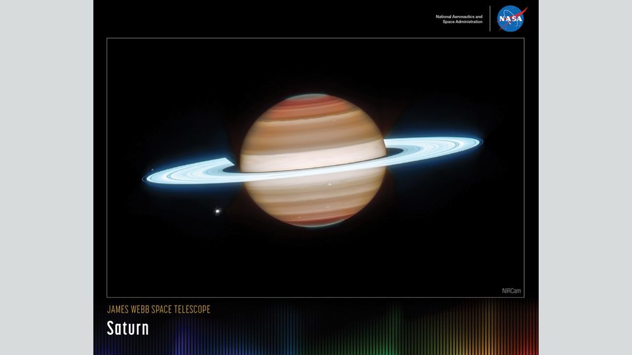 A rectangular poster with an image of Saturn (with Dione, seen as a bright dot to Saturn’s bottom left) against a black background. Saturn’s body is mostly composed of different layers of brown. Both of Saturn’s poles have a dark brown color, which gradually transitions to a lighter brown toward Saturn’s center. Saturn is surrounded by several bright, sky-blue rings. These rings are mostly broad, with a few singular narrow gaps between the broader rings. Along the bottom is a series of thin vertical bars ranging from purple at left to blue, green, yellow, orange, and red at right. Bars are separated slightly, with black in between. Bar colors are brightest at the bottom, fading up to black. Brightness varies from bar to bar, giving the array an undulating feel. At upper right is text that reads, “National Aeronautics and Space Administration” and NASA’s blue, white, and red meatball insignia. Title text appears at lower left that reads, “James Webb Space Telescope: Saturn.”