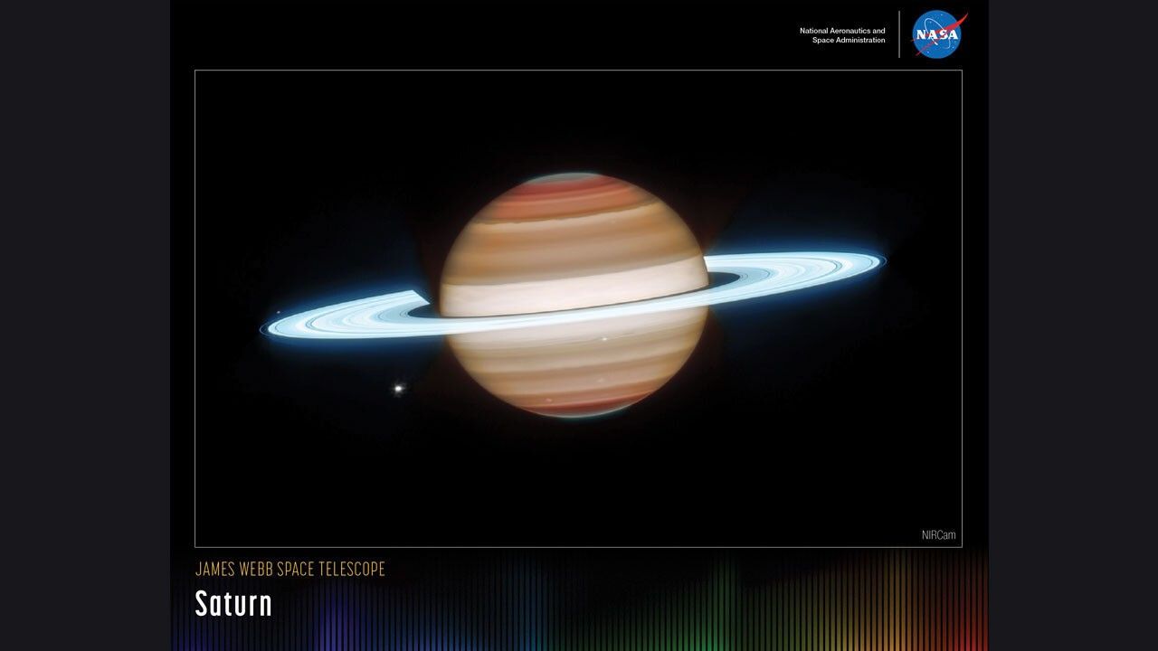 A rectangular poster with an image of Saturn (with Dione, seen as a bright dot to Saturn’s bottom left) against a black background. Saturn’s body is mostly composed of different layers of brown. Both of Saturn’s poles have a dark brown color, which gradually transitions to a lighter brown toward Saturn’s center. Saturn is surrounded by several bright, sky-blue rings. These rings are mostly broad, with a few singular narrow gaps between the broader rings. Along the bottom is a series of thin vertical bars ranging from purple at left to blue, green, yellow, orange, and red at right. Bars are separated slightly, with black in between. Bar colors are brightest at the bottom, fading up to black. Brightness varies from bar to bar, giving the array an undulating feel. At upper right is text that reads, "National Aeronautics and Space Administration" and NASA’s blue, white, and red meatball insignia. Title text appears at lower left that reads, "James Webb Space Telescope: Saturn."