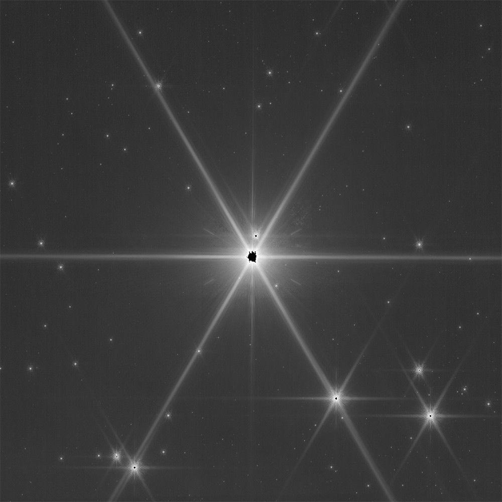 A bright star appears at center with eight white diffraction spikes. The background is black. The core of the star is also black.