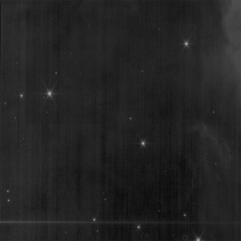 A black-and-white image shows a few white stars in the scene. Irregular, light gray vertical lines known as striations appear all across the image.