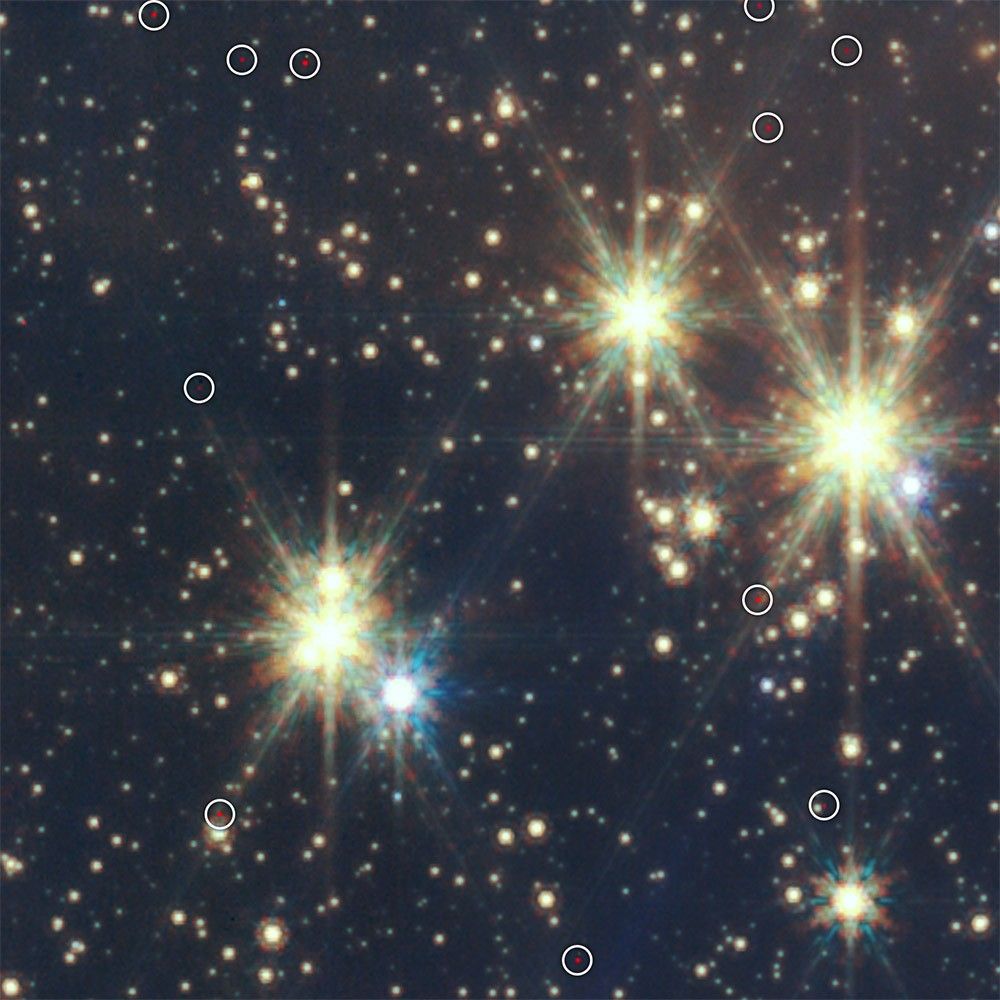 The background is dark gray, and there are light yellow stars of all sizes in the scene. Tiny red dots toward the top, middle, and bottom of the image have white circles to show the cosmic rays that are removed from Webb’s images.