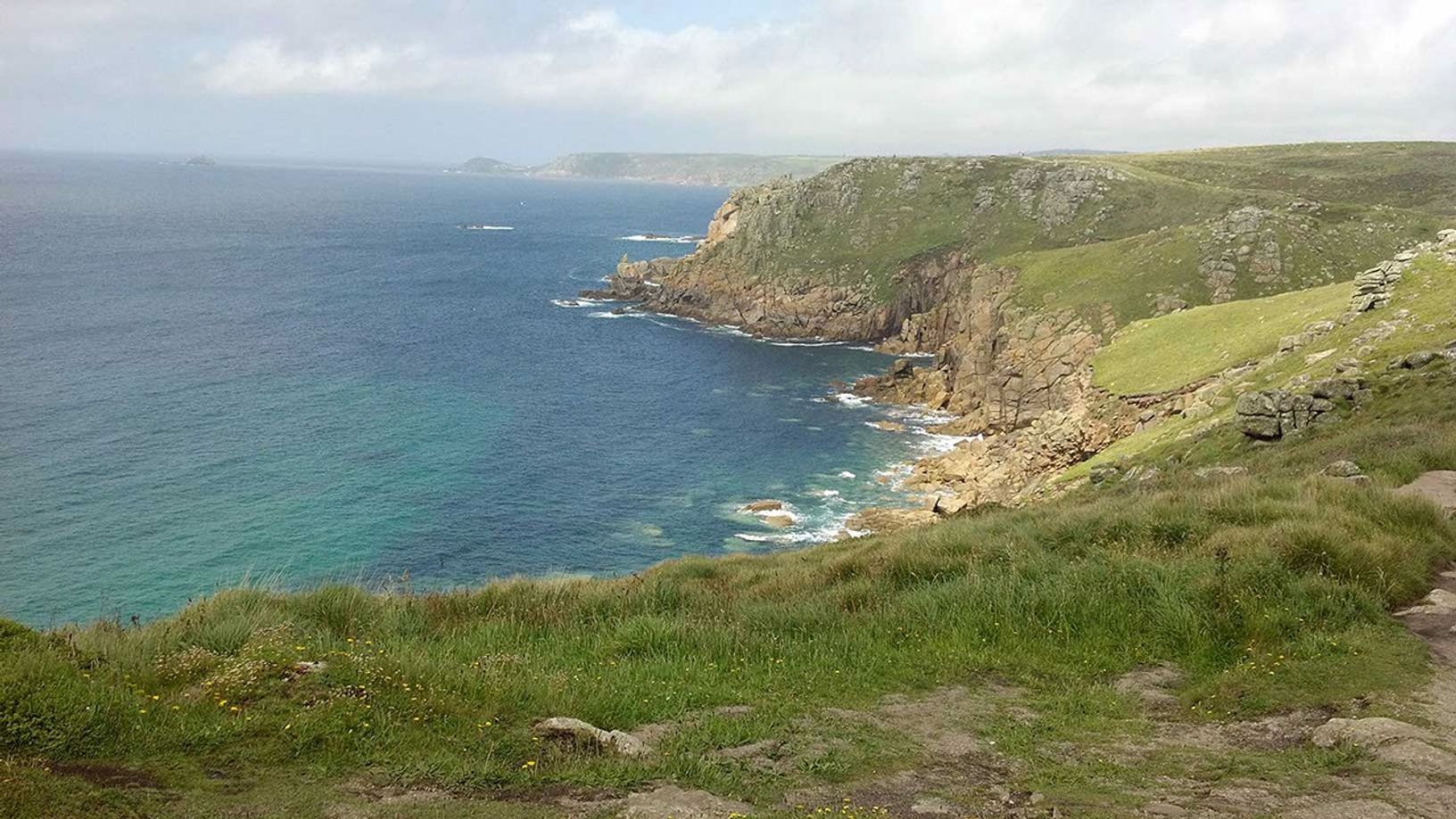 Blue-green water, brown rock, grey clouds, green plants