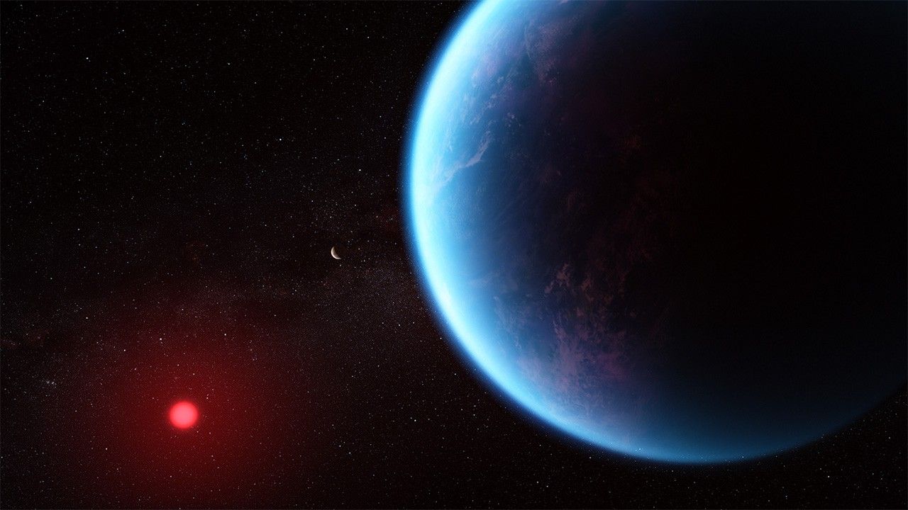 Illustration of a planet and its cool red dwarf star. In the foreground on the right is the planet, which fills most of the frame. The planet is various shades of blue, with wisps of white scattered throughout. The left edge of the planet (the side facing the star) is lit, while the rest is in shadow. In the background at the lower left is the star, which appears smaller. The star has a bright red glow. Also in the background is another planet, which appears as a small crescent. The black background of space is speckled with a few small stars.