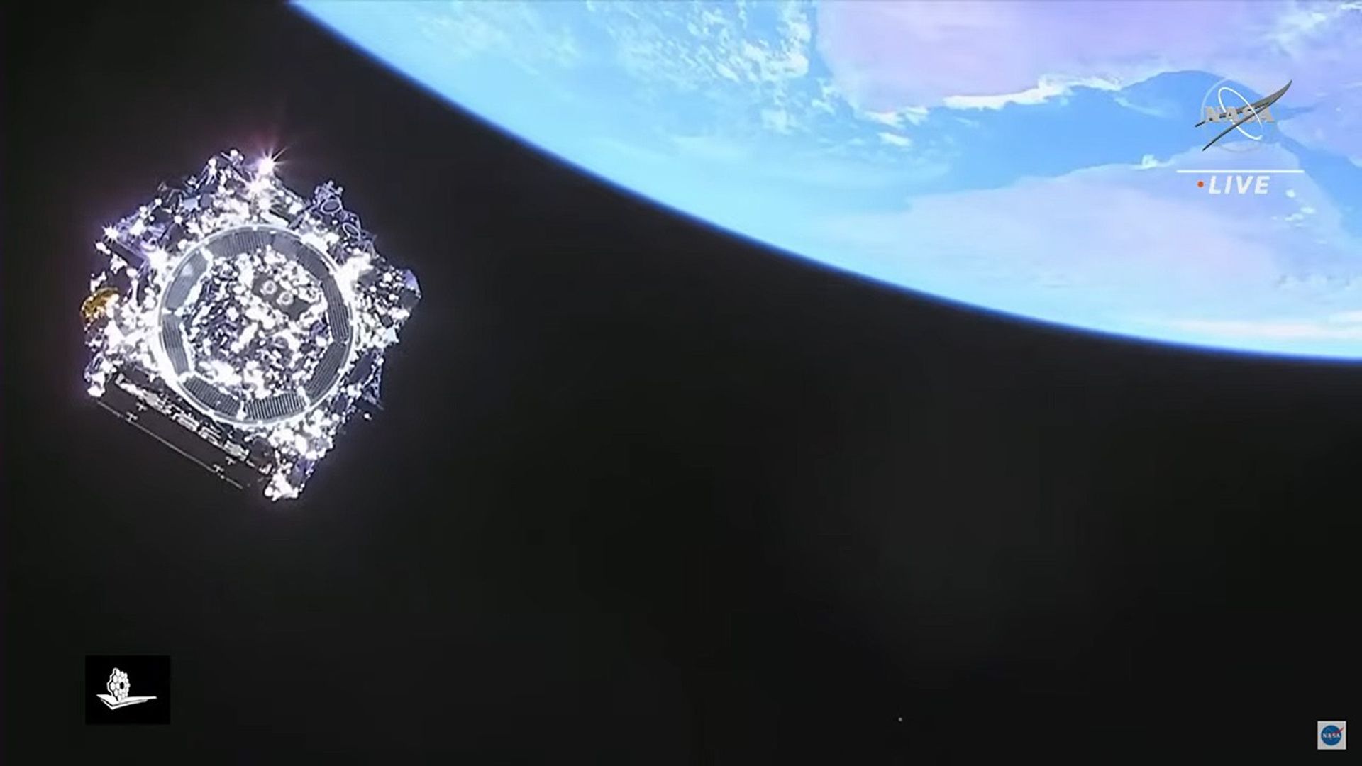 View of the bottom of NASA’s James Webb Space Telescope, after separation from the rocket, at top left. A large portion of Earth appears in the top right corner. Still folded up, Webb is a shiny, metallic-colored square with many small pieces, some of which are glinting in the sunlight. A pared-down NASA logo appears over Earth at top right, with LIVE written beneath it. A small, flattened white Webb graphic appears at bottom left and the NASA “meatball” logo at bottom right. The background of space is black.