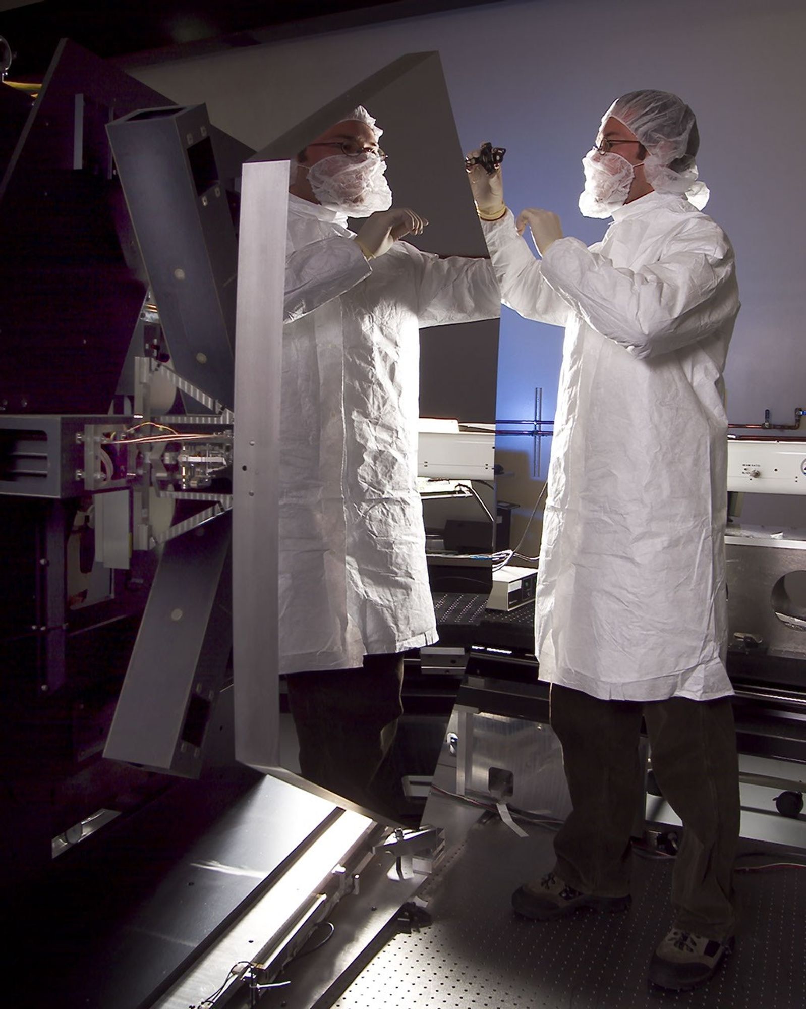 A specialists, wearing a white protective "bunny suit," inspects a hexagon-shaped segment of Webb's beryllium mirror.