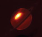 Saturn as seen in mid-infrared light. Near the north pole of the planet, a bright irregular oval is set off in bright white at the center, and fades to yellow and bright red toward the edges.
