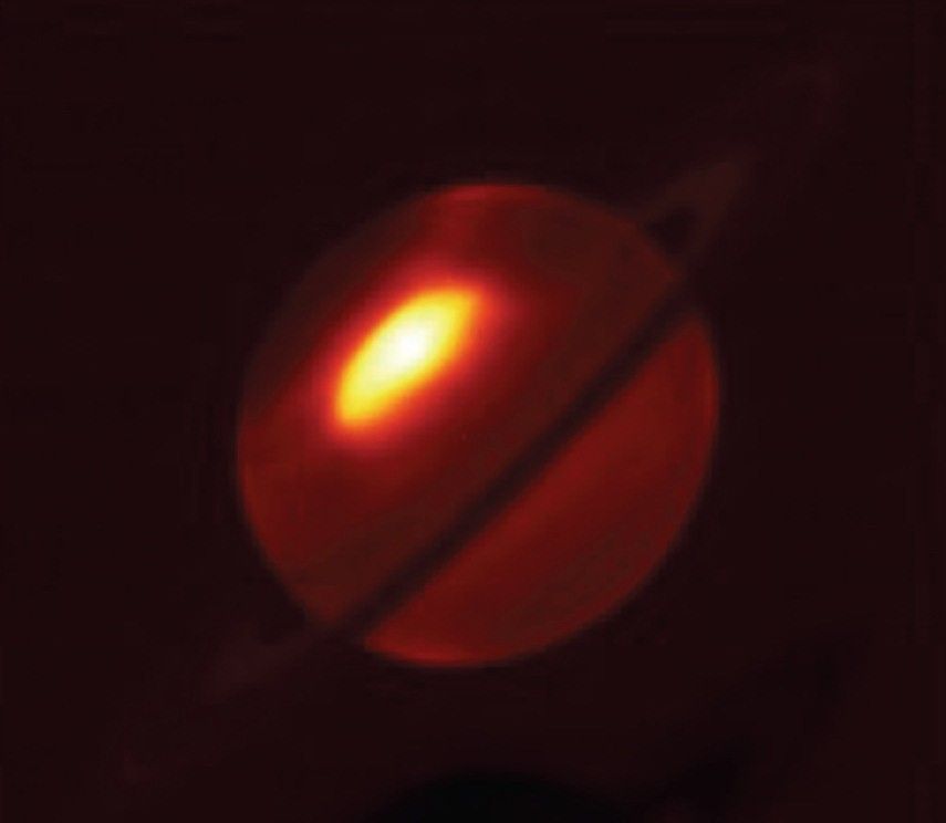 Saturn as seen in mid-infrared light. Near the north pole of the planet, a bright irregular oval is set off in bright white at the center, and fades to yellow and bright red toward the edges.