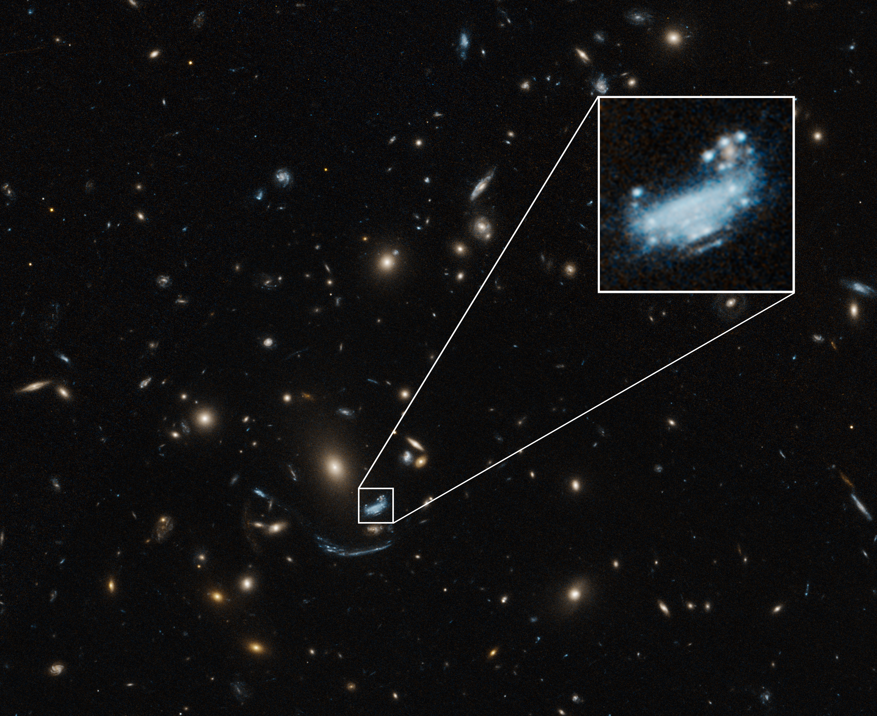 A largely black image is covered with blue, white, yellow, and orange dots of various sizes throughout. Toward the bottom center, a blue galaxy is highlighted by a small white square, which is enlarged near the top right corner.