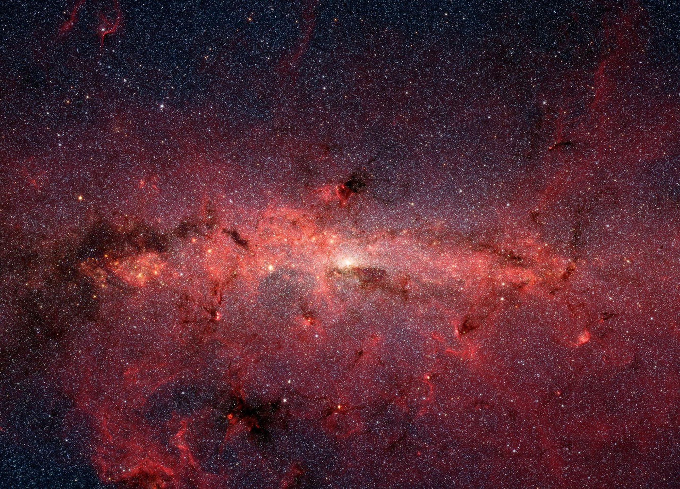 The center of our Milky Way galaxy, shown in shades of red, nearly fills the entire image with stars, gas, and dust.