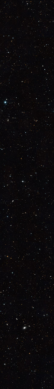 Thin horizontal Hubble image of tens of thousands of distant galaxies set against the black background of space. Most appear only as tiny dots in shades of red, orange, and white.