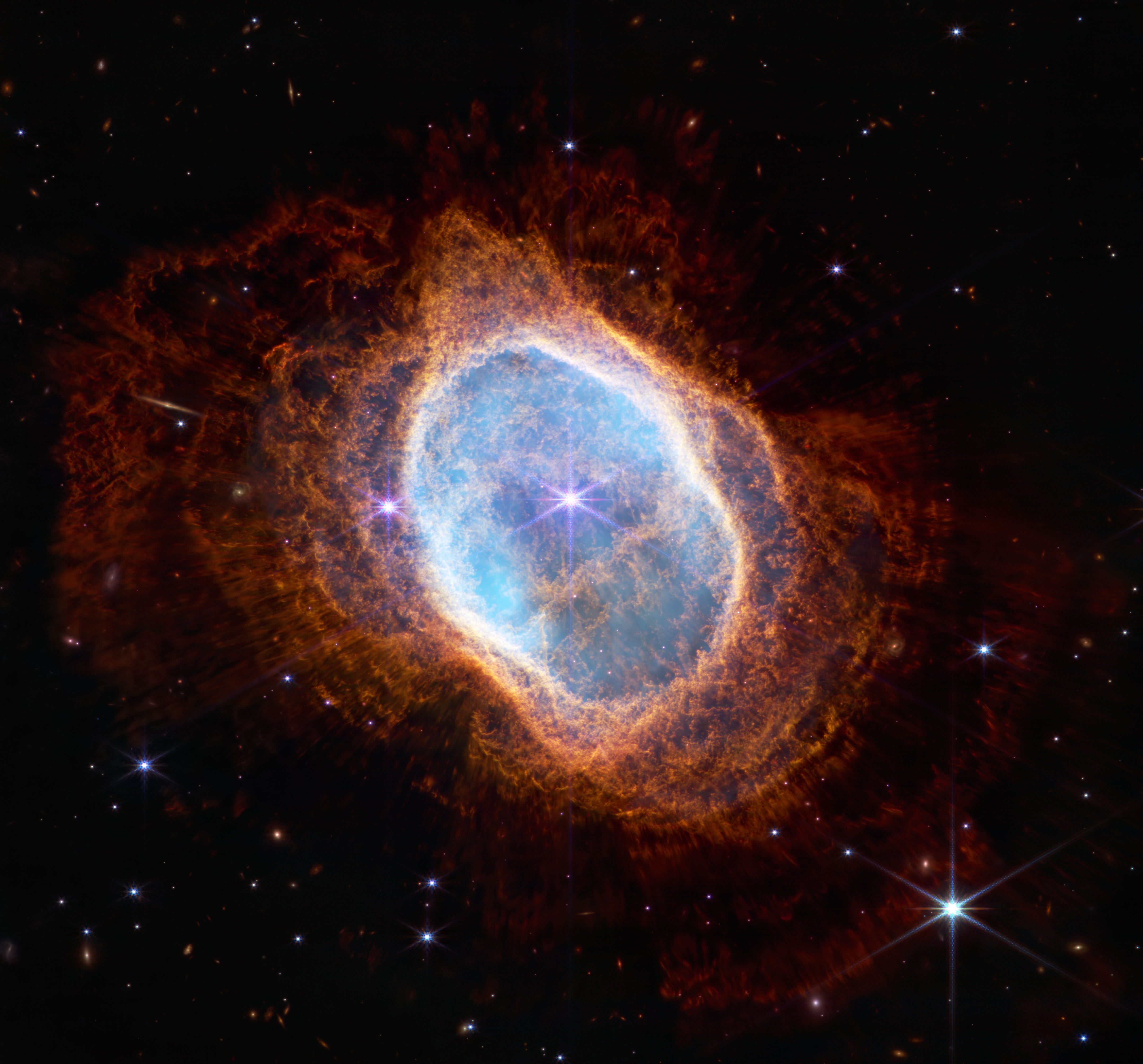 Colorful image of near-infrared light from a glowing cloud with a distorted ring-like shape, illuminated from within by a bright central star.
