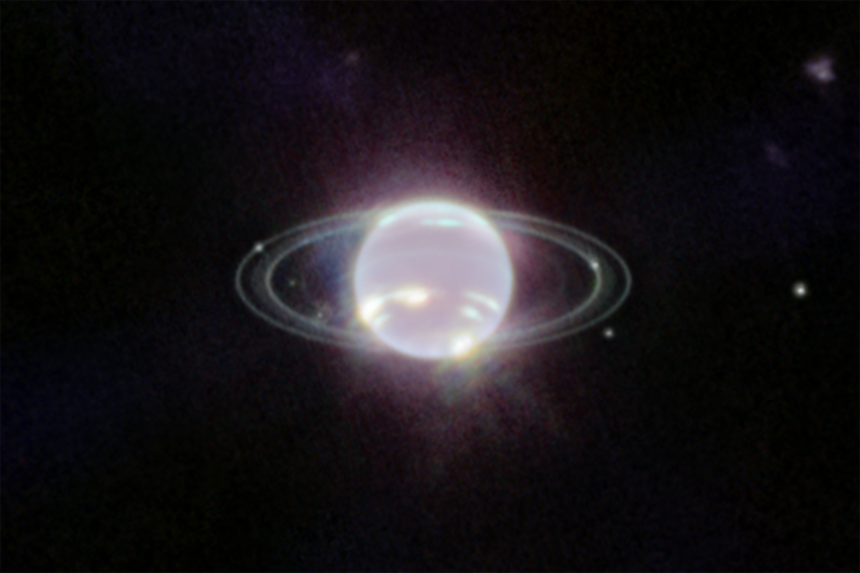 Image has a mostly dark background and at the center of the image is a glowing sphere, mostly white, almost neon, with a few extremely bright patches of methane-ice clouds splattered throughout the sphere’s bottom half. The glowing sphere is accompanied by several narrow, faint rings— 2 thinner, crisper rings and 2 broader, fainter rings. There are 6 tiny white dots, some floating among the black background near the sphere, others placed among the rings. These are 6 of Neptune’s 14 moons. In the top right corner of the image is a very dim splotch.