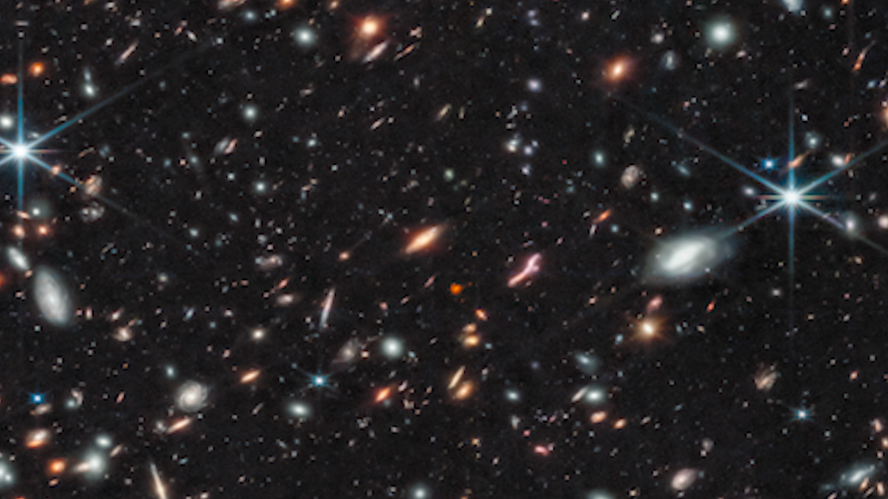 A field of hundreds of galaxies of different shapes, sizes and colors. A handful of bright stars display 8 diffraction spikes.
