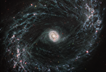 A large galaxy takes up the entirety of the image. The image is mostly black with a bright, glowing oval core at the center. The core is mostly bright white, but there are also swirling, detailed structures that resemble water circling a drain. There is white and light blue colored dust that emanates from the core’s center, but it is tightly contained to the core. There is black space between the core and glowing dust of the outer oval rings. The rings are wispy and highlight filaments of dust around cavernous black bubbles. The dust in the outer rings contains dots that are navy blue, pinkish, reddish, and white. Throughout, there is also a smattering of background galaxies seen as small red and greenish dots.