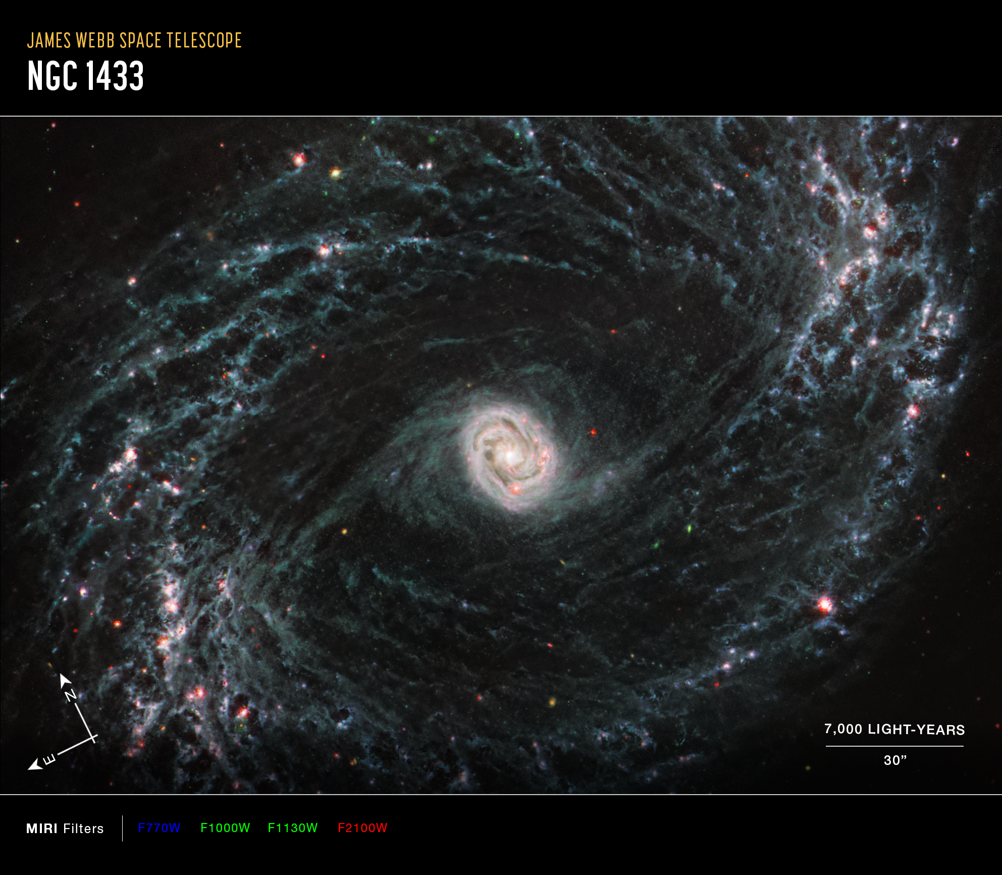 A large galaxy takes up the entirety of the image. The image is mostly black with a bright, glowing oval core at the center. The core is mostly bright white, but there are also swirling, detailed structures that resemble water circling a drain. There is white and light blue colored dust that emanates from the core’s center, but it is tightly contained to the core. There is black space between the core and glowing dust of the outer oval rings. The rings are wispy and highlight filaments of dust around cavernous black bubbles. The dust in the outer rings contains dots that are navy blue, pinkish, reddish, and white. Throughout, there is also a smattering of background galaxies seen as small red and greenish dots.