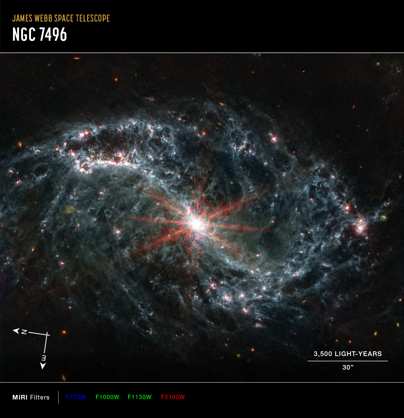 A large galaxy takes up the entirety of the image. The image is mostly black, with a bright, glowing circular core at the center. Six reddish diffraction spikes extend from the core. The spiral arms of the galaxy outstretch to the upper left and the lower right. There is black space between the core and the main spiral arms of the galaxy. Those arms are wispy and highlight filaments of dust around cavernous black bubbles. That dust in the outer rings contains diffuse dots that are navy blue, pinkish, reddish, and white. Throughout, there is also a smattering of background galaxies seen as small red and greenish dots.