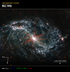 A large galaxy takes up the entirety of the image. The image is mostly black, with a bright, glowing circular core at the center. Six reddish diffraction spikes extend from the core. The spiral arms of the galaxy outstretch to the upper left and the lower right. There is black space between the core and the main spiral arms of the galaxy. Those arms are wispy and highlight filaments of dust around cavernous black bubbles. That dust in the outer rings contains diffuse dots that are navy blue, pinkish, reddish, and white. Throughout, there is also a smattering of background galaxies seen as small red and greenish dots.